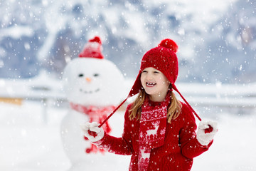 Child building snowman. Kids build snow man.