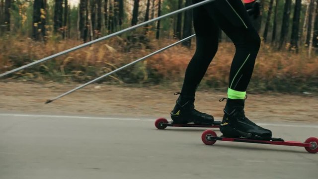 Training an athlete on the roller skaters. Biathlon ride on the roller skis with ski poles, in the helmet. Autumn workout. Roller sport. Adult man riding on skates. Shooting an athlete in motion