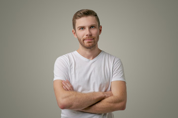 Portrait of a stylish hipster wearing a white t-shirt posing indoors with arms crossed, having a sullen expression on face. Isolated studio shot, horizontal