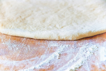 Making homemade pizza in a country kitchen with an overhead view of rolled out dough for the base with a wooden rolling pin on oven paper on an old wooden chopping board