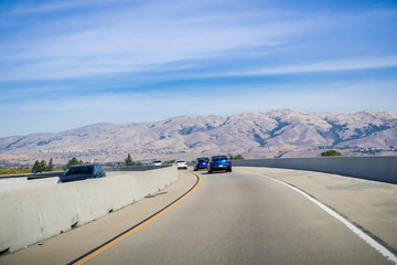 Driving on the express lane to switch between highways; Mission peak, Monument peak and Allison peak in the background; Milpitas, south San Francisco bay, California