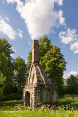 Fototapeta na wymiar Abandoned ruin of oven chimney. Broken furnace. Green meadow environment and blue sky background