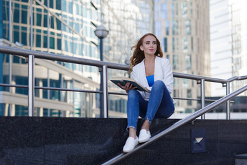 Beautiful girl sitting on the steps and reading a book between skyscrapers