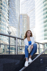 Beautiful girl sitting on the steps and reading a book between skyscrapers