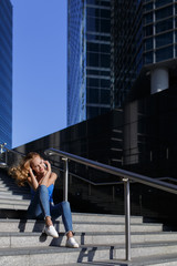 Beautiful girl sitting on the steps with her smartphone between skyscrapers