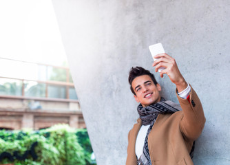 Outdoor portrait of modern young man with mobile phone in the street making a selfie