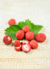Freeze dried whole and pieces of strawberries on green strawberry leaf, healthy snack full of vitamins and nutrition on natural wooden background. Preserving berries for winter concept.