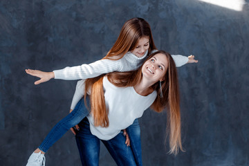 Stylish beautiful mother and a cute daughter with blue eyes in studio hugging and having fun. family, love concept