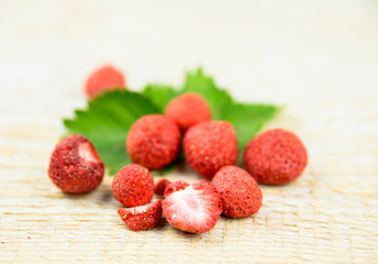 Freeze dried whole and pieces of strawberries on green strawberry leaf, healthy snack full of vitamins and nutrition on natural wooden background. Preserving berries for winter concept.