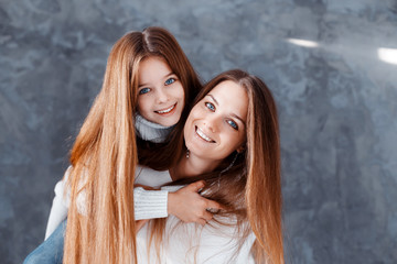 Stylish beautiful mother and a cute daughter with blue eyes in studio hugging and having fun. family, love concept