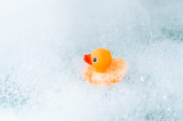 Orange playful rubber duck on the edge of the bath, blue bubble background. Children's washing...