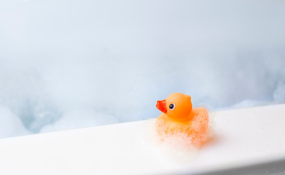 Orange playful rubber duck on the edge of the bath, blue bubble background. Children's washing concept. Children`s pool area concept. Room for text.