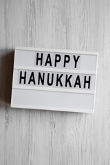 Obraz premium 'Happy Hanukkah' word on modern board over white wooden background, overhead view. From above, flat lay, top view.