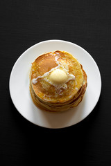 Stack of homemade pancakes with butter on white plate on black table, top view. Overhead, from above.