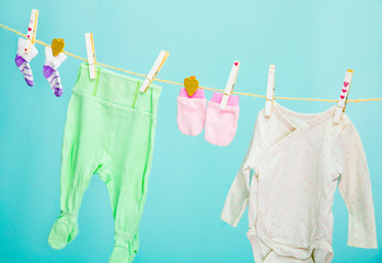 Fresh washed newborn baby clothes dry on clothes line, closed with clothes pins isolated on blue background.