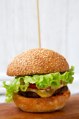 Homemade cheeseburger on wooden board over white wooden background, side view. Closeup.