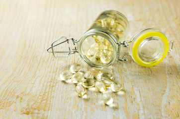 Close up of nice yellow vitamin D capsules and a glass jar with capsules on background, on wooden background.