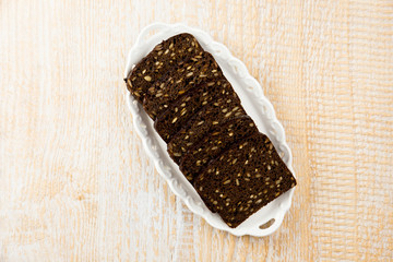 Black bread with sunflower seeds on a white fancy tray on light wooden background. Bread made with rye flour. Very healthy. Popular in Eastern Europe.