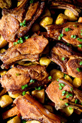 Oven baked pork with oven baked potatoes on black oven pan, homemade.