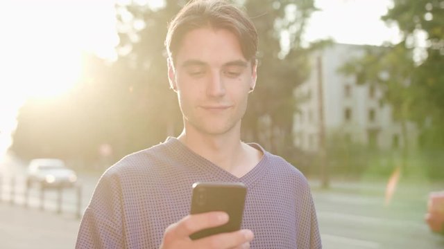 An attractive young man using a phone in town. Close-up shot. Soft focus. Lens flare