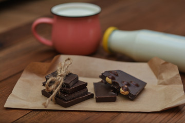Handmade chocolate pieces, cup and bottle with milk on wooden background.