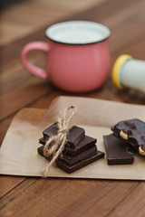 Handmade chocolate pieces on rustic paper, a cup and a bottle with milk on a wooden background. Delicious breakfast - milk and chocolate.