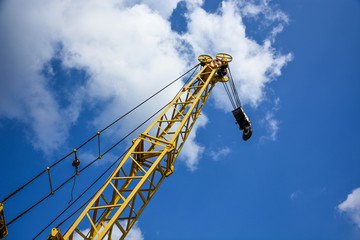 Yellow crane, with a hook for lifting, loading against the blue sky with clouds.