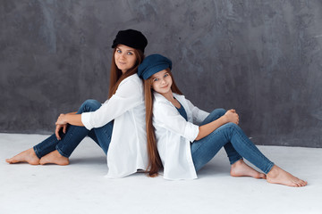 Stylish beautiful mother and a cute daughter with blue eyes in studio hugging and having fun. mom and daughter wearing  hats