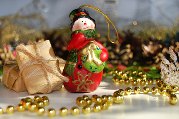 Christmas background. A toy ceramic snowman, a toy ceramic hut, boxes of gifts, golden beads, cones. Christmas background.