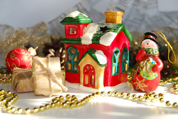 Christmas background. A toy ceramic snowman, a toy ceramic hut, boxes of gifts, golden beads, cones. Christmas background.