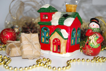 Christmas background. A toy ceramic snowman, a toy ceramic hut, boxes of gifts, golden beads, cones. Christmas background.