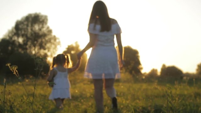 Backlight bright sun shining at mommy holding daughter's hand going across grass