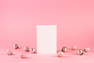 Mock up with vertical invitation card on trendy pastel light pink background with christmas ornaments. Greeting card and silver Christmas baubles. Minimal christmas concept.