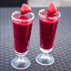 Two glasses of red berry juice on a table with sugar coating and strawberry decoration