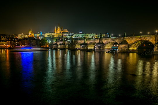 Night view of famous Prague castle, capital of Czech Republic, medieval stone bridge with statues and street lights, Charles bridge, colorful reflection in water of red, blue, yellow and white colors