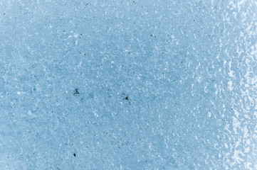 A close-up of the surface of a fragment of a glacier with a structure of strips and bubbles interspersed with sand and rocky rock. Ice blue texture to the light. Small DOF