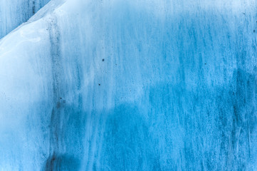 Close-up wall of a centuries-old glacier with a structure of stripes and bubbles. Ice blue light texture