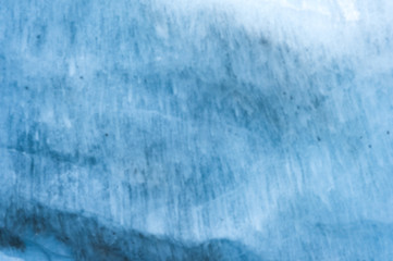Close-up blurred wall of a centuries-old glacier with a structure of stripes and bubbles. Ice blue light texture