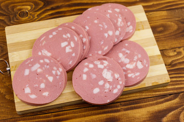 Sliced boiled sausage on cutting board on wooden table