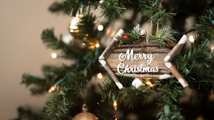 Seasonal Idea of Festive Holiday Photo with Cute Wooden Arrow Ornament with Merry Christmas in Script Font inside Christmas Tree with Bright White Lights and Gold Ornaments with Blurred Background 