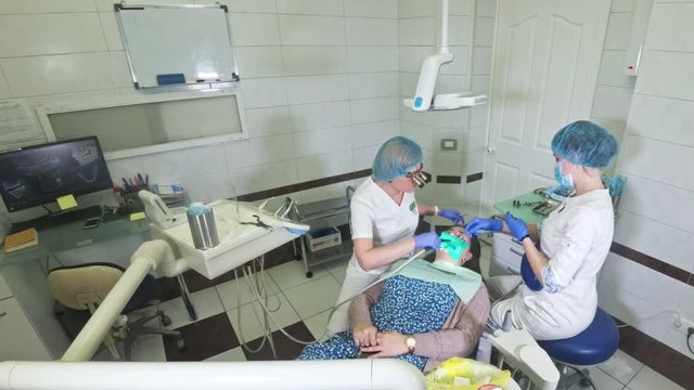Woman at dentist clinic gets dental treatment to fill a cavity in a tooth. Dental restoration and composite material polymerization with UV light and laser. Shooting at a wide angle.