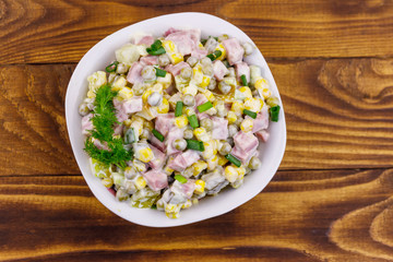 Tasty salad with sausage, green pea, canned corn, bell pepper, cucumber and mayonnaise on wooden table. Top view