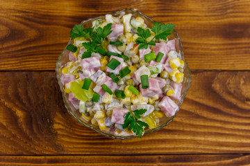 Tasty salad with sausage, green pea, canned corn, bell pepper, cucumber and mayonnaise on wooden table. Top view