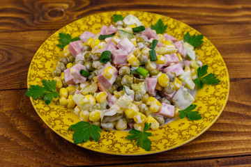 Tasty salad with sausage, green pea, canned corn, bell pepper, cucumber and mayonnaise on wooden table