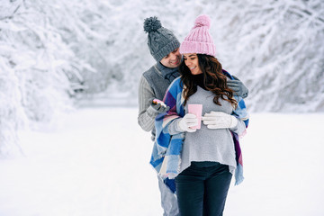 Fototapeta na wymiar Young man hugs his pregnant wife gently while walking in a snowy park. Family love and care concept.