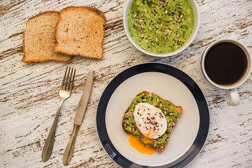 Food photography of an avocado toast with poached egg, sesame seeds, and black coffee. Breakfast, lunch, brunch, light dinner dish meal, vegetarian food, healthy eating concept.