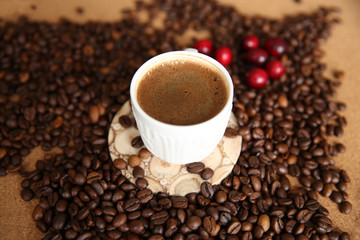 cup of coffee and coffee beans with red berries on wooden background