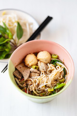 Spicy rice noodles soup in a bowl with chopsticks and fresh vegetables, Thai food