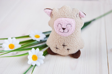 handmade soft toy lamb on a light wooden background, artificial flowers, grass