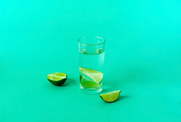 Glass with water and lime on green background. Detox concept. Copy space, close up.